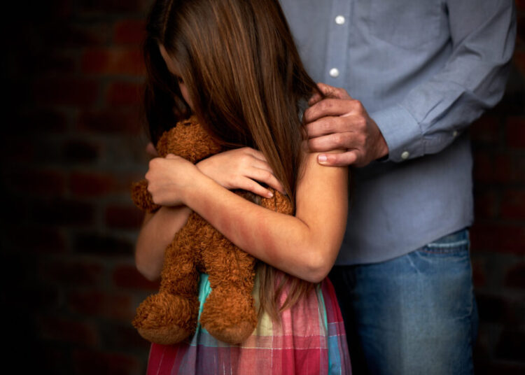 Innocence lost. Abused little girl with her abuser gripping her shoulder